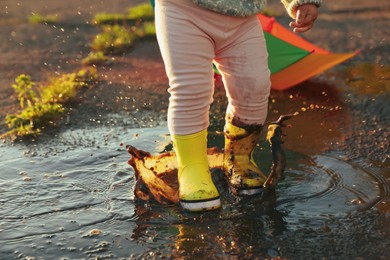 Little girl wearing rubber boots walking in puddle outdoors, closeup and space for text