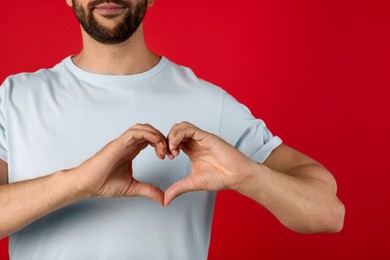 Man making heart with hands on red background, closeup