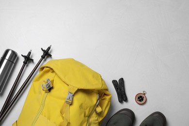 Flat lay composition with trekking poles and other hiking equipment on light background, space for text