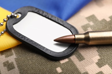 Military ID tag, bullet and Ukrainian flag on pixel camouflage, closeup