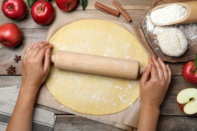 Woman rolling dough for apple pie at wooden table, top view