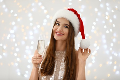 Happy young woman in Santa hat with champagne against blurred Christmas lights