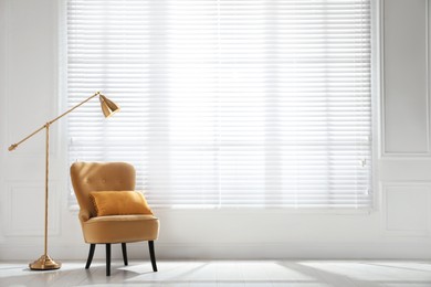 Cosy armchair and floor lamp near large window with blinds in spacious room. Interior design