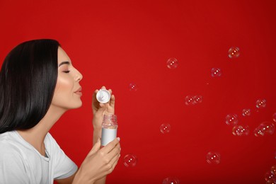Photo of Young woman blowing soap bubbles on red background, space for text