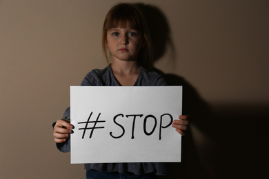 Photo of Abused little girl with hashtag STOP near beige wall. Domestic violence concept