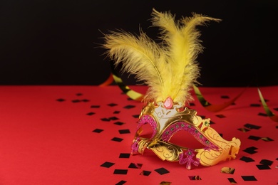Beautiful golden carnival mask and shiny confetti on red table. Space for text