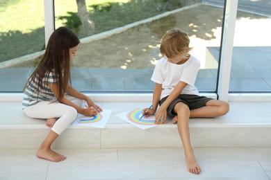Little children drawing rainbows near window indoors. Stay at home concept