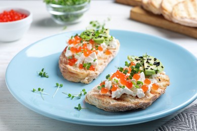 Delicious sandwiches with caviar, cheese, avocado and microgreens on white wooden table