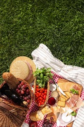 Picnic blanket with different products on green grass, top view. Space for text