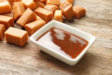 Delicious caramel candies and sauce on wooden background