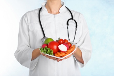 Female doctor with fresh products on light background. Cardiac diet