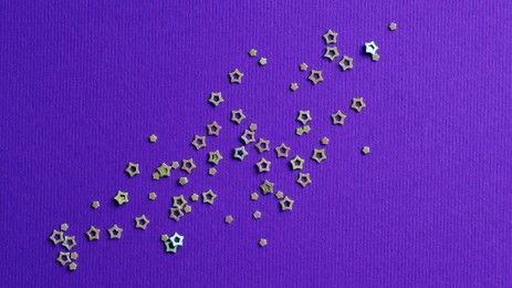 Many silver star shaped sequins on purple background, flat lay