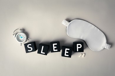 Word Sleep, alarm clock, pills and mask on light grey table, flat lay. Insomnia treatment