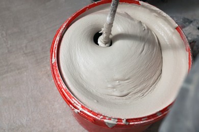 Mixing putty with electric mixer in red bucket indoors, above view