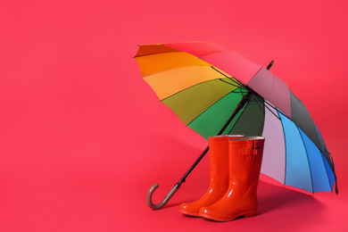Colorful umbrella and rubber boots on red background. Space for text