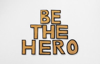 Phrase Be The Hero made of cardboard letters on white background, flat lay