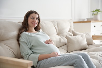 Happy pregnant woman touching her belly indoors