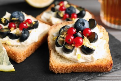 Tasty sandwiches with cream cheese, blueberries, red currants and lemon zest on slate plate, closeup