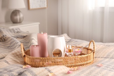 Aroma lamp, bottle of oil and burning candles on wicker tray in bedroom