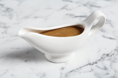 Delicious turkey gravy in sauce boat on white marble table