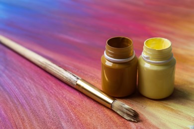 Jars with paints and brush on abstract picture, closeup