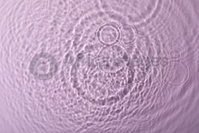 Photo of Clear water with rippled surface on pink background, top view