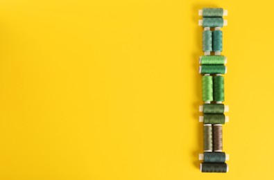 Photo of Different shades of green sewing threads on yellow background, flat lay. Space for text