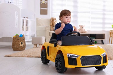 Photo of Adorable child with cookie driving yellow toy car in room