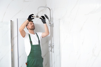 Professional handyman working in shower booth indoors, space for text