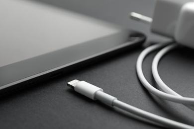 Tablet and USB charge cable on black background, closeup. Modern technology