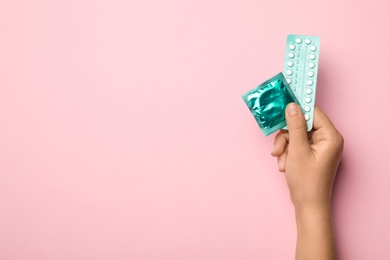 Woman holding condom and birth control pills on pink background, top view with space for text. Safe sex