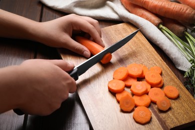 Photo of Woman cutting tasty carrot at brown wooden table, closeup