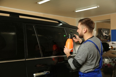 Skilled worker washing tinted car window in shop