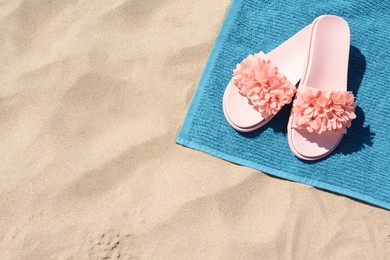Photo of Towel and stylish flip flops on sand, above view with space for text. Beach accessories