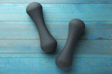 Photo of Two dumbbells on light blue wooden table, flat lay