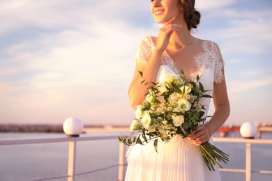Gorgeous bride in beautiful wedding dress with bouquet near river, closeup