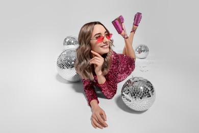 Photo of Beautiful woman in sunglasses and sequin dress among disco balls on white background