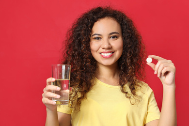 Photo of African-American woman with glass of water and vitamin pill on red background