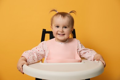 Cute little baby wearing bib in highchair on yellow background