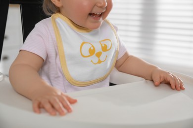 Cute little baby wearing bib in highchair at home, closeup
