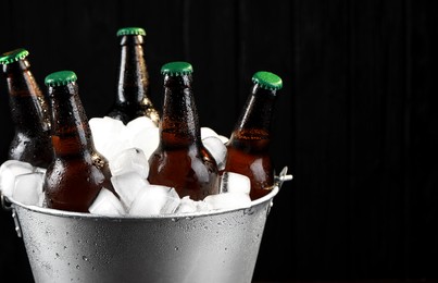 Photo of Metal bucket with bottles of beer and ice cubes on dark wooden background, closeup
