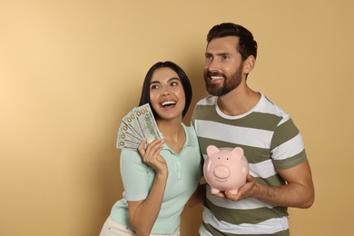 Happy couple with money and ceramic piggy bank on beige background