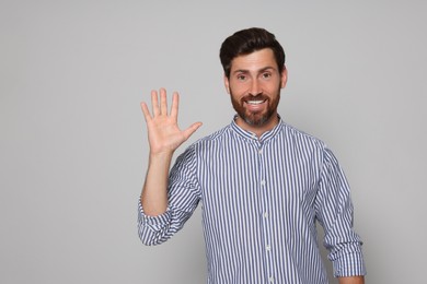 Photo of Portrait of smiling bearded man showing hand on grey background. Space for text