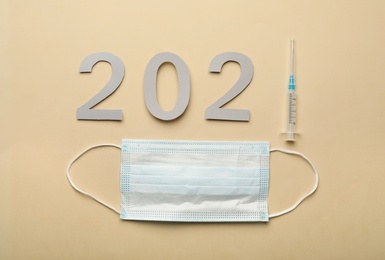 Paper numbers with syringe forming 2021 and medical mask on beige background, flat lay. Coronavirus vaccination