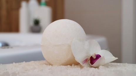 Bath bomb with orchid and sea salt on table in bathroom, closeup