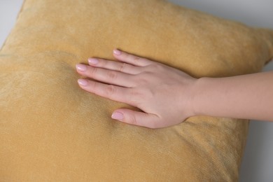 Photo of Woman touching soft yellow pillow on bed, closeup