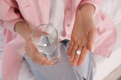 Young woman with abortion pill and glass of water on bed, closeup