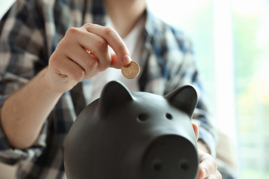 Man putting coin into piggy bank against blurred background, closeup