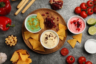 Different kinds of tasty hummus served with nachos on grey table, flat lay
