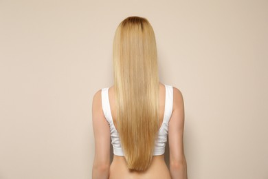 Young woman with long straight hair on beige background, back view